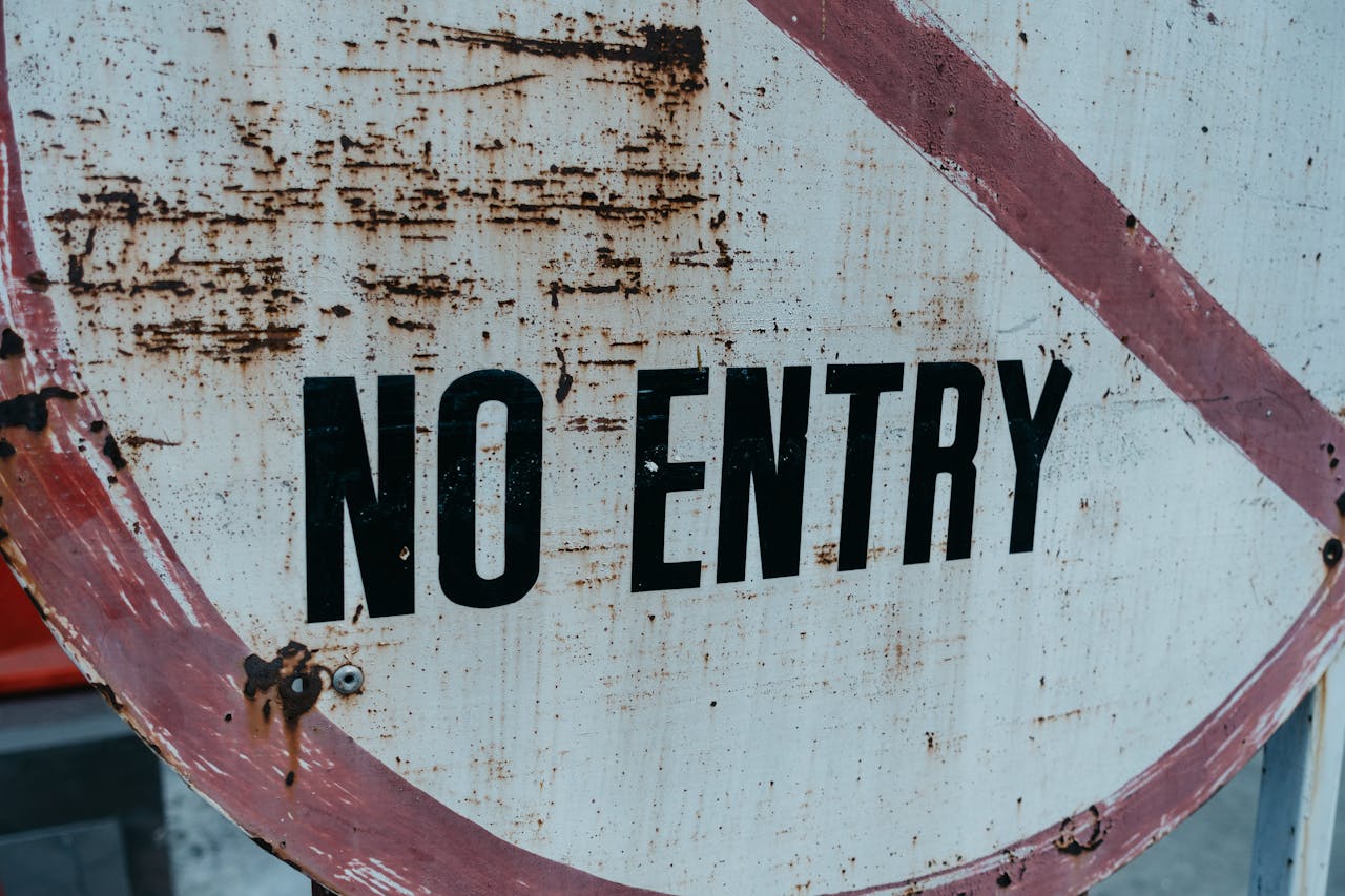 A close-up of a weathered and rusty no entry sign with red and white paint.