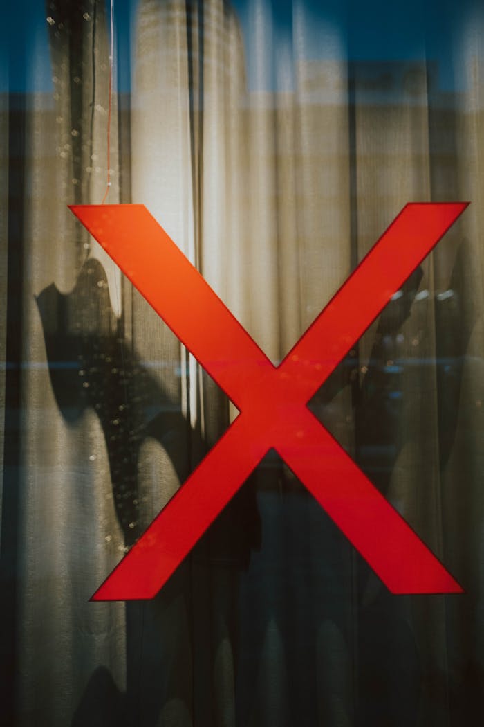 A striking red X on a glass window with intriguing shadows behind, creating a mysterious scene.