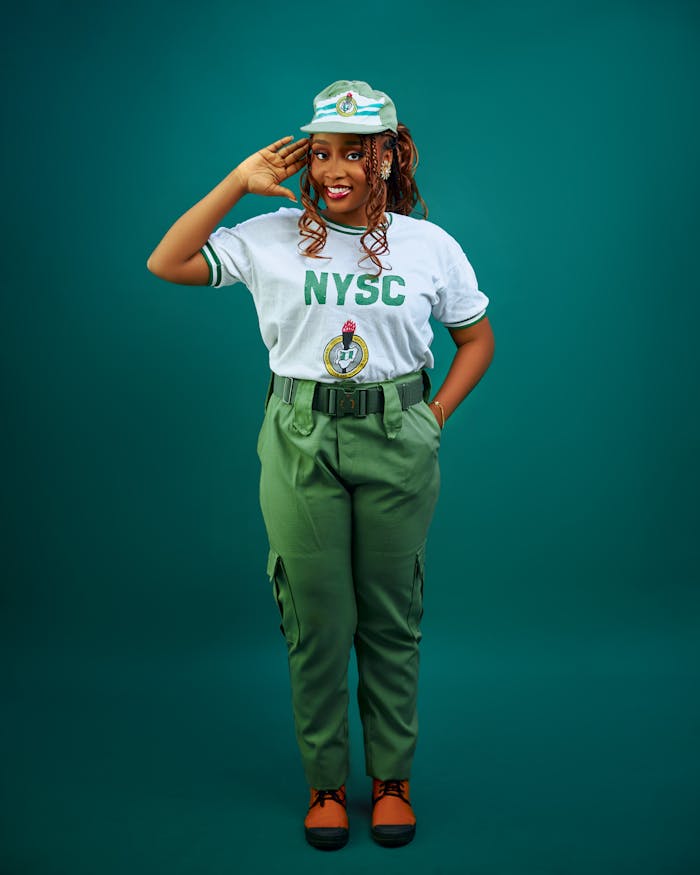 Crafting Captivating Headlines: Your awesome post title goes here Confident young woman in NYSC uniform giving a salute on a solid green background.