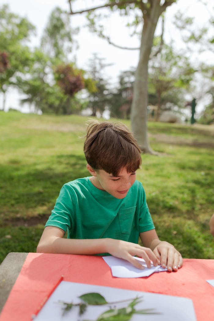 A child enjoying paper crafts in a sunny park setting, surrounded by greenery.