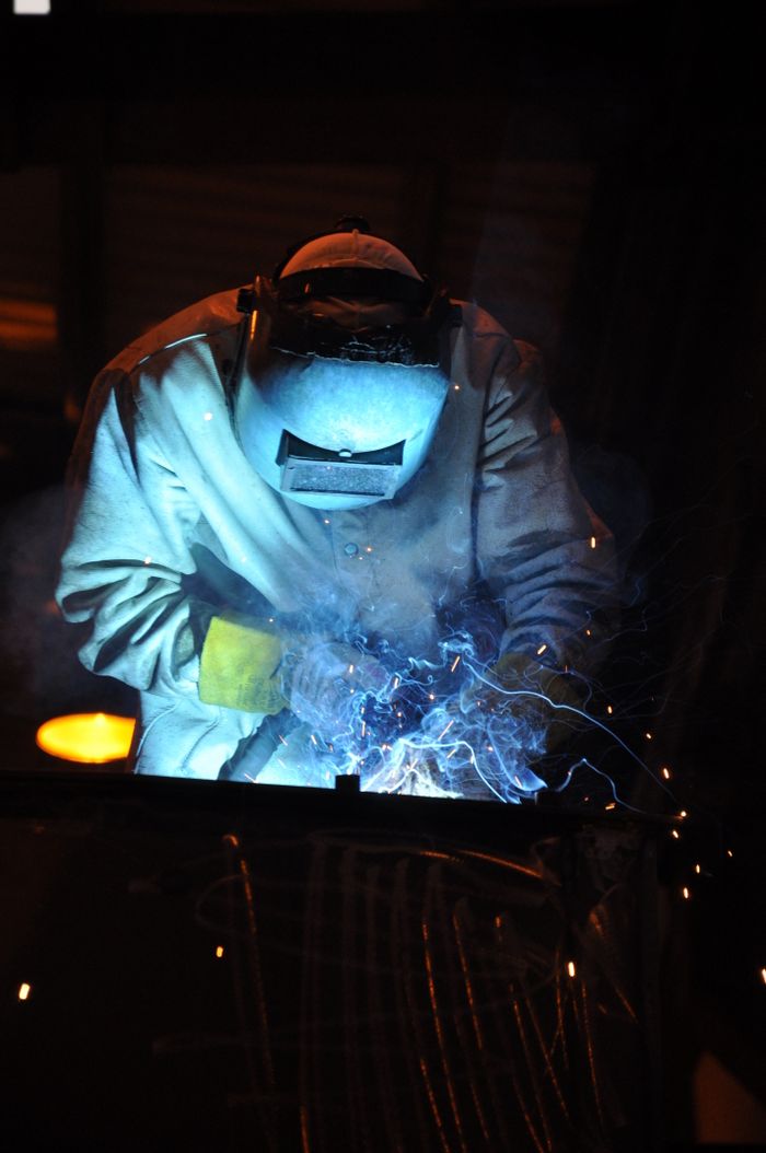 A skilled welder working in a dark workshop with blue sparks flying, showcasing metalworking expertise.